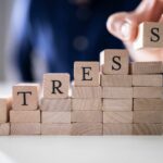 Mano che posiziona un cubo di legno con la lettera “S” sopra una pila di blocchi che formano la parola “stress"