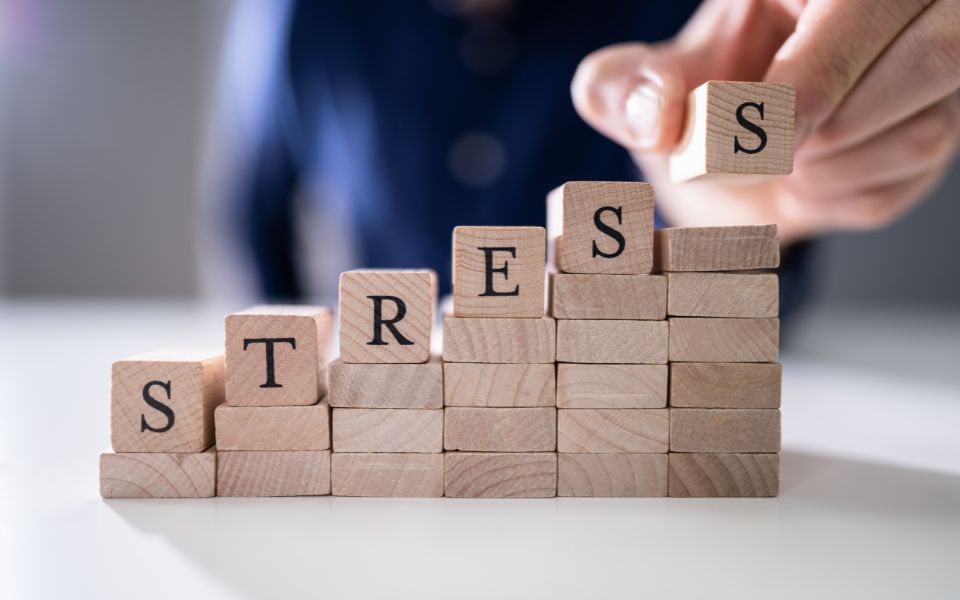 Mano che posiziona un cubo di legno con la lettera “S” sopra una pila di blocchi che formano la parola “stress"